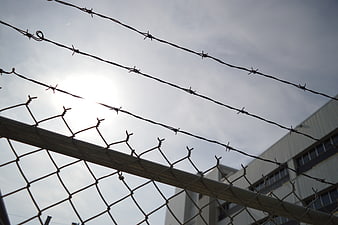 Barbed wire and chain link fence against cloudy sky