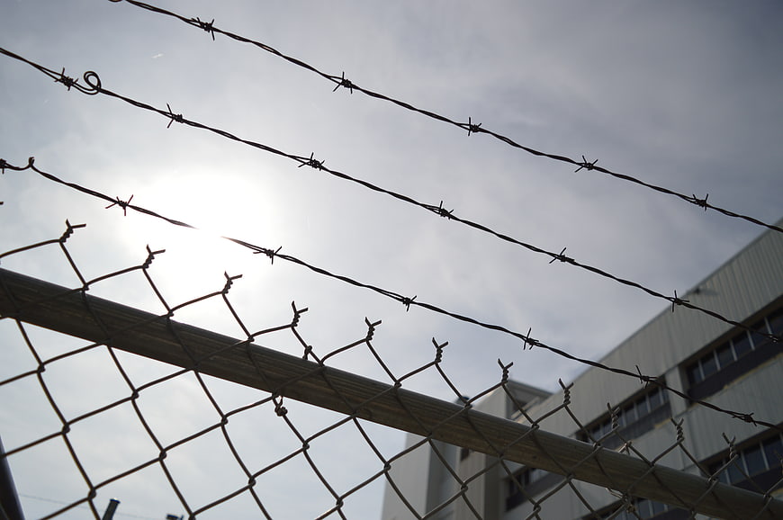 Barbed wire and chain link fence against cloudy sky