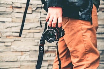 Hand holding Sony Alpha camera against stone wall background