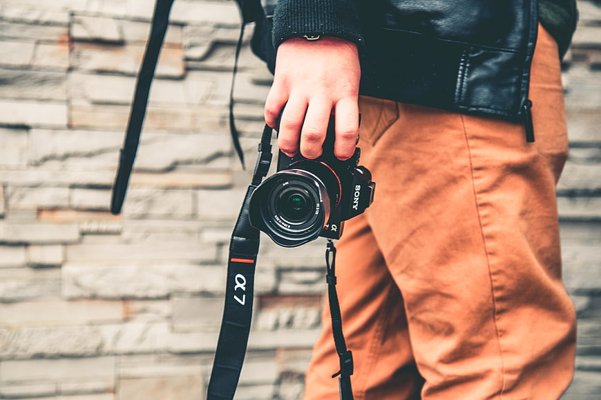 Hand holding Sony Alpha camera against stone wall background
