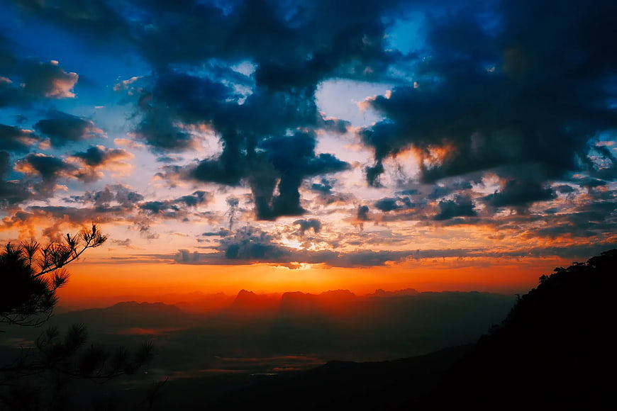 Dramatic Sunset Over Mountain Range with Silhouetted Trees