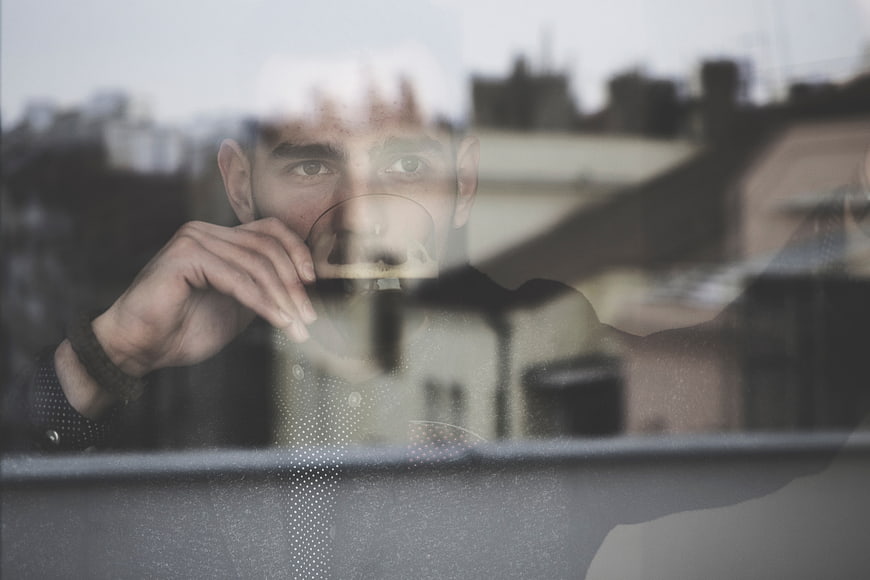 Man drinking coffee looking through window with city reflection