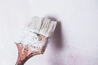 Close-up of paintbrush applying white paint to textured wall