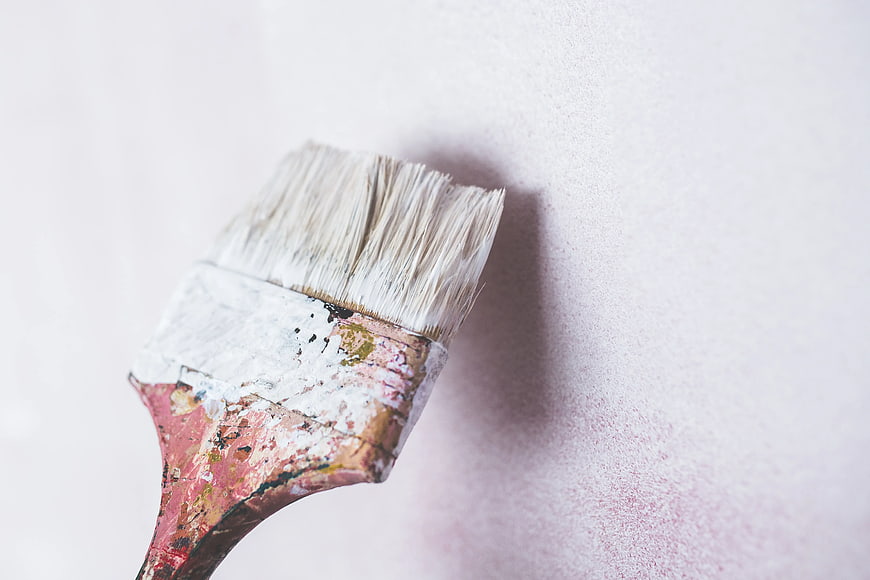 Close-up of paintbrush applying white paint to textured wall