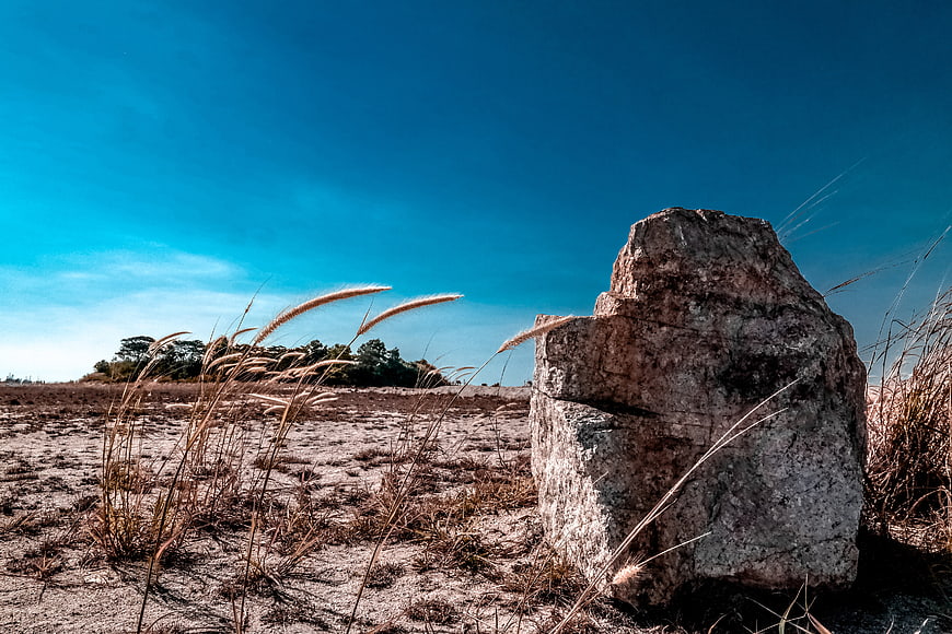 Large Rock in Dry Grassland Under Blue Sky
