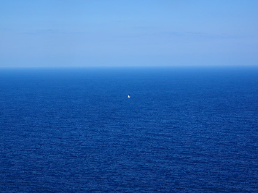 Lone Sailboat on Vast Blue Ocean Horizon