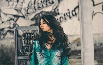 Woman with long dark hair in denim shirt against graffiti wall