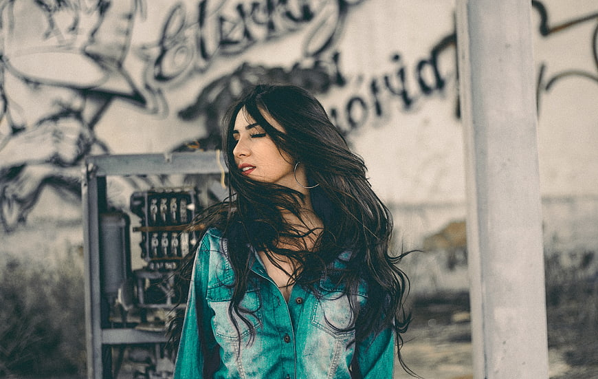 Woman with long dark hair in denim shirt against graffiti wall
