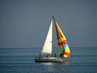 Sailboat with colorful spinnaker sailing on calm blue sea