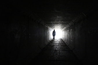 Silhouette of a person walking toward light in a dark concrete tunnel