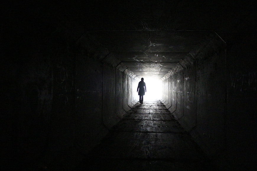 Silhouette of a person walking toward light in a dark concrete tunnel
