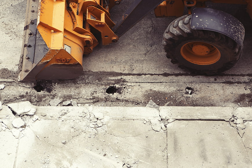 Yellow construction loader breaking concrete pavement