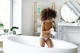 Cute child with curly hair playing with soap in bathtub