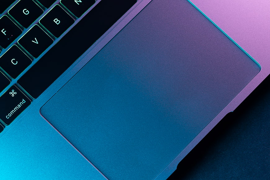Close-up of laptop keyboard and trackpad with neon blue and purple lighting