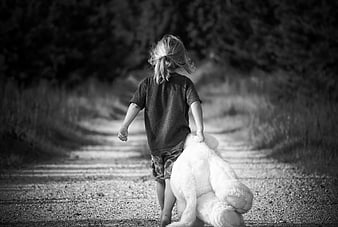 Child walking on gravel path dragging large white teddy bear