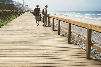 Two men walking on a sunny wooden boardwalk by the beach
