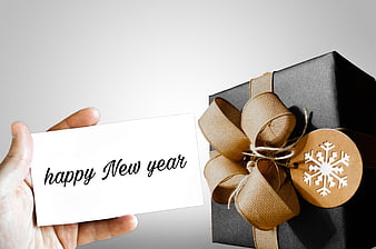 Hand holding happy new year card next to black gift box with burlap bow
