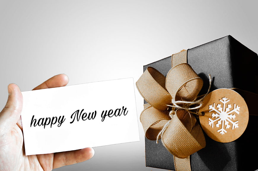 Hand holding happy new year card next to black gift box with burlap bow