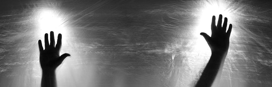 Silhouette of hands reaching toward bright light through textured surface