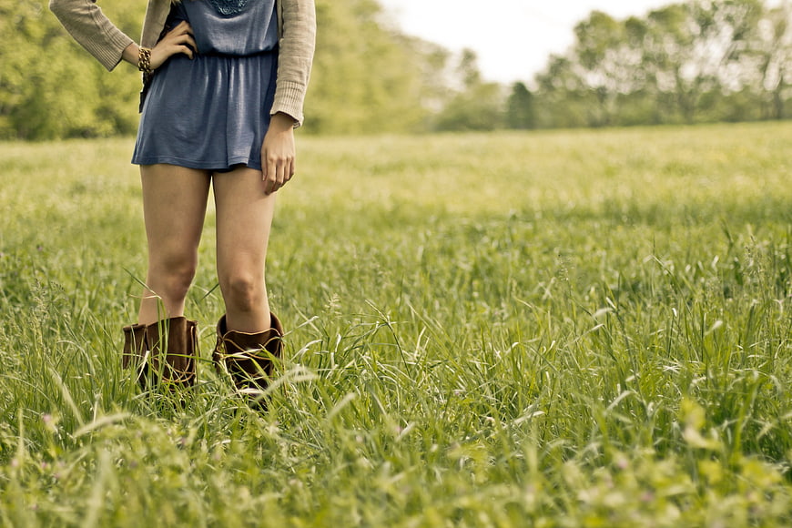 Woman in blue skirt and brown boots standing in green meadow
