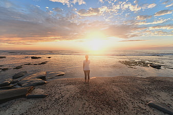 Woman standing on beach watching golden sunset over ocean