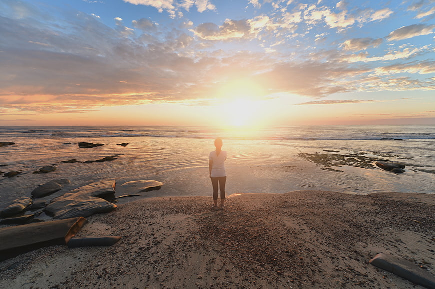 Woman standing on beach watching golden sunset over ocean