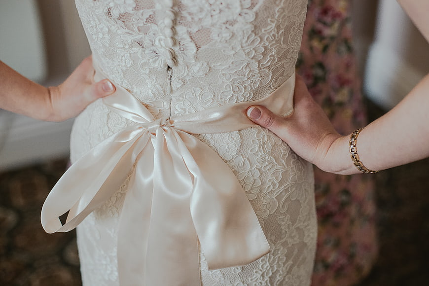 Hands tying satin sash on lace wedding dress