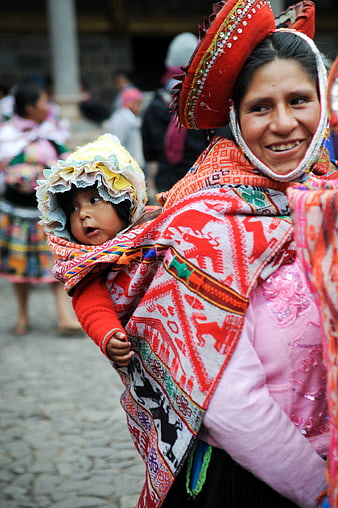 Peruvian woman in traditional dress carrying baby in market