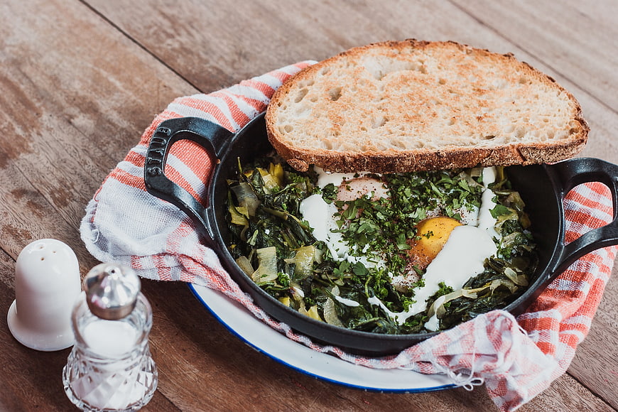 Shakshuka with greens and toast in cast iron skillet