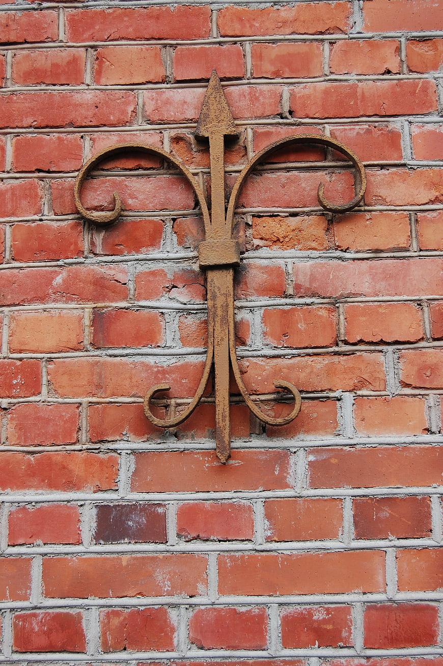 Rusty Wrought Iron Fleur-de-lis on Red Brick Wall