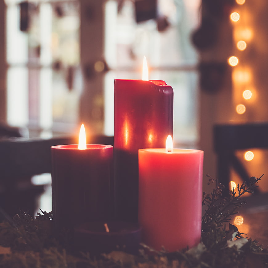 Three lit red candles with festive greenery and bokeh lights