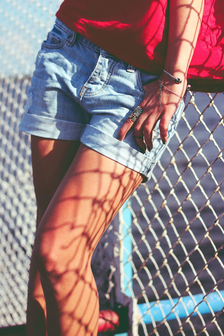 Woman in denim shorts with chain-link fence shadows