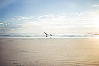 Surfers walking on sandy beach at sunset