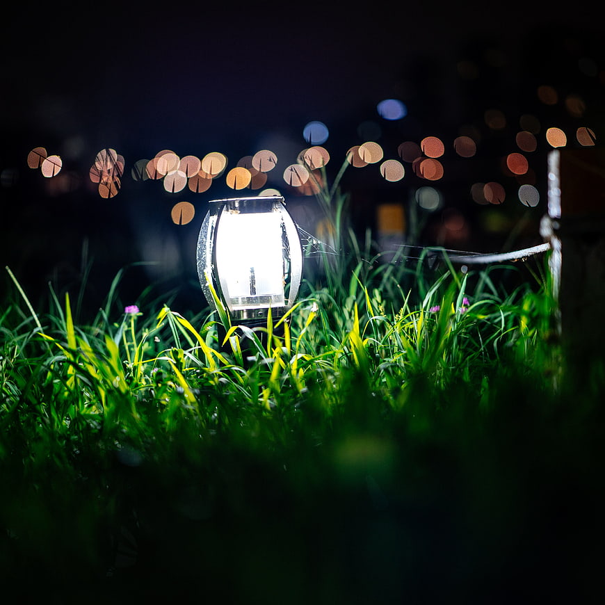 Glowing Solar Lantern in Green Grass at Night with Bokeh