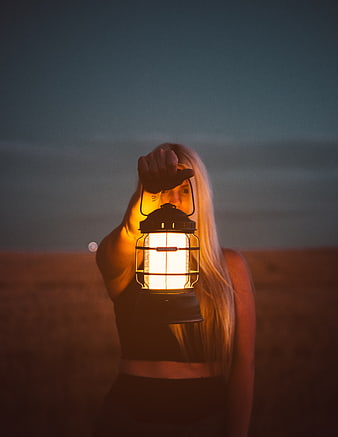 Woman holding glowing lantern in field at dusk