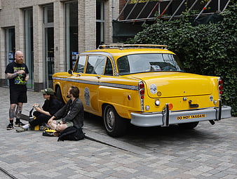 Vintage yellow taxi parked on city street with people