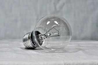 Clear incandescent light bulb lying on white textured fabric