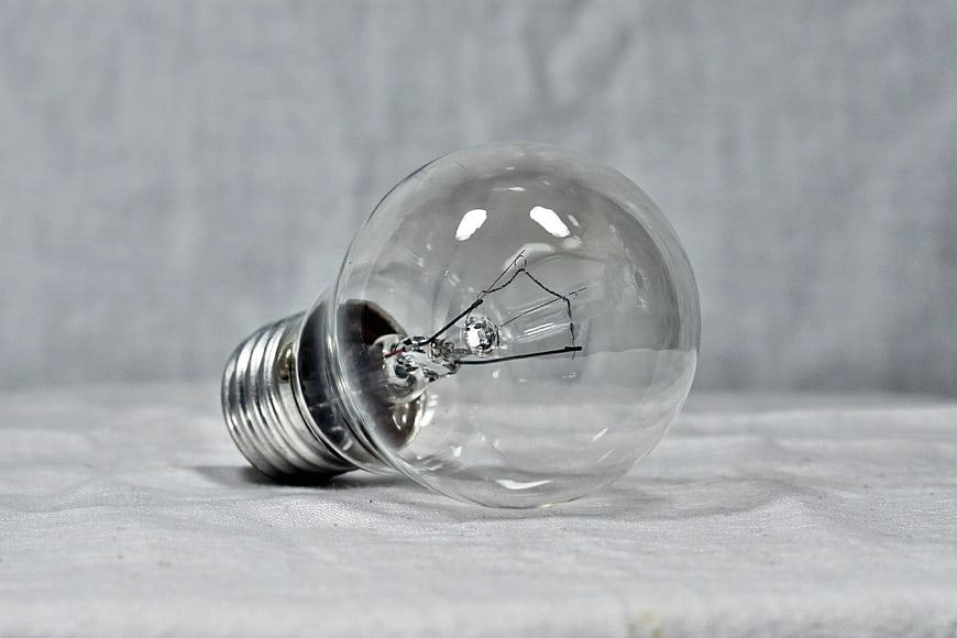 Clear incandescent light bulb lying on white textured fabric