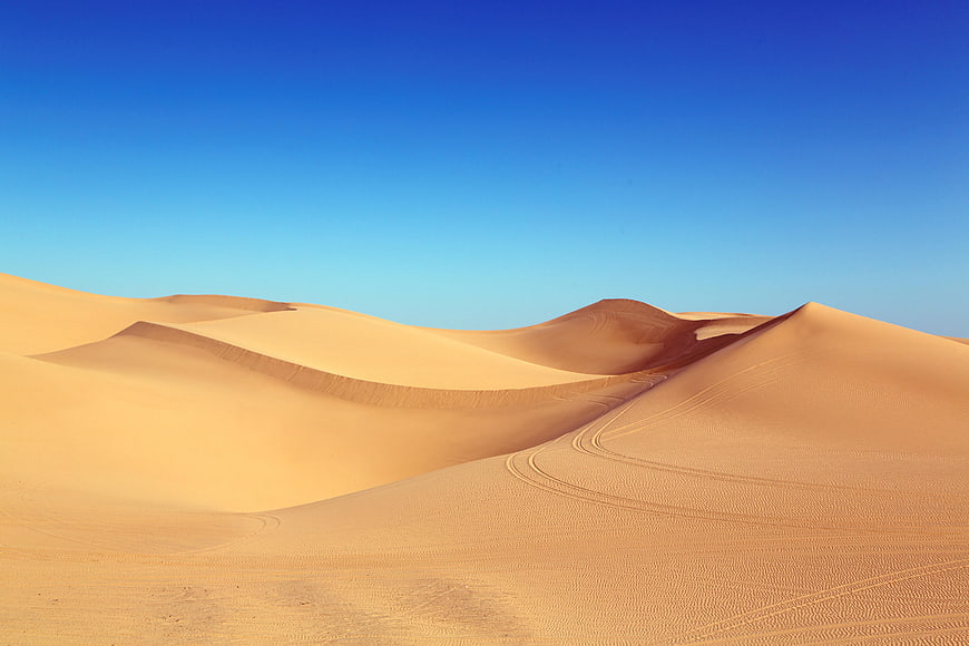 Golden sand dunes with tire tracks under clear blue sky
