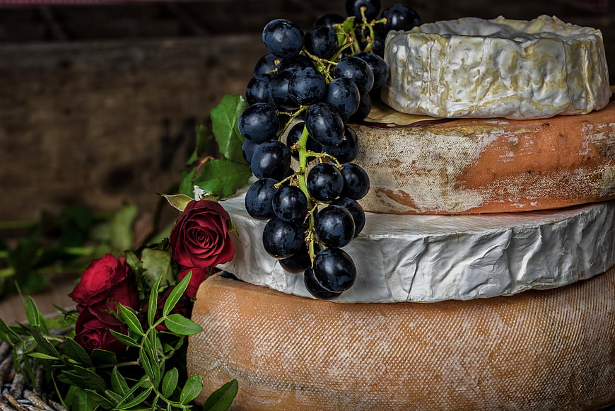 Stack of artisanal cheese wheels with grapes and red roses