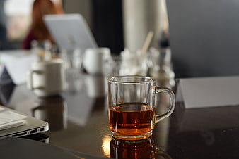 Glass cup of tea on office desk with blurred background