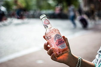 Hand holding bottle of rose lemonade outdoors