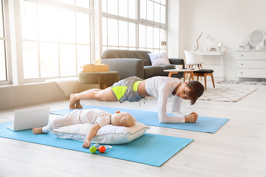Mother doing yoga plank while baby sleeps on mat