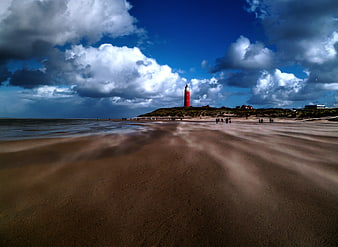 Red Lighthouse on Sandy Beach with Dramatic Clouds