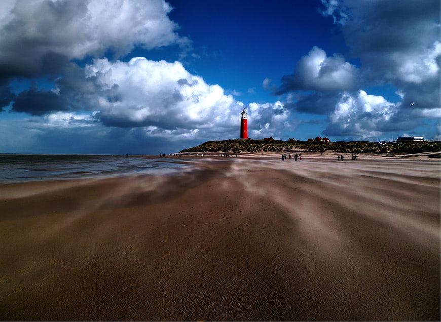 Red Lighthouse on Sandy Beach with Dramatic Clouds