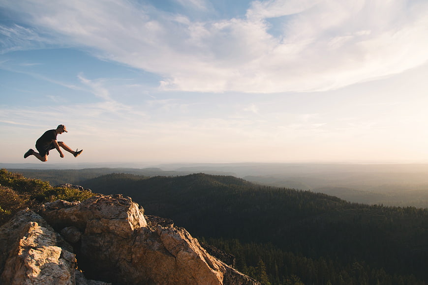 Man jumping off mountain cliff at sunrise