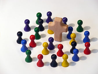 Wooden Cross Surrounded by Colorful Game Pieces on White Background