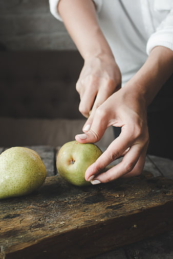 Hands cutting fresh pear on rustic wooden board