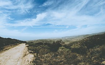 Dirt Road Winding Through Hills Under Blue Sky