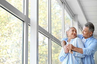Happy senior couple embracing by large window